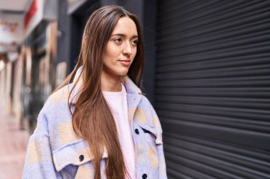 Young beautiful hispanic woman looking to the side with serious expression at street