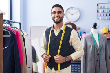 Genç Arap terzi gülümseyerek giyim fabrikasında duruyor.