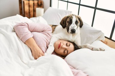 Genç bir kadın yatak odasında bir köpekle yatakta uyuyor.