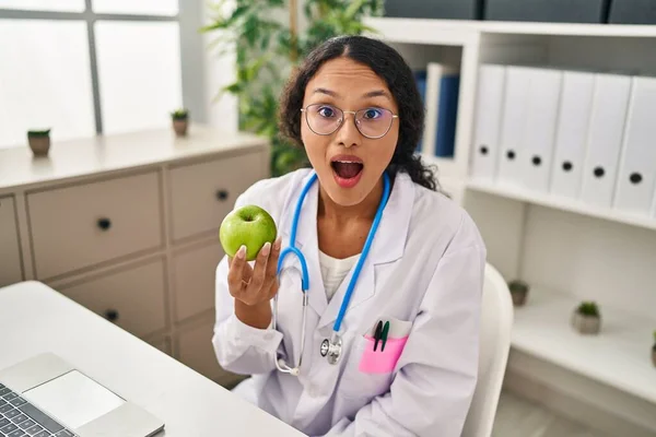 年轻的惊慌失措的医生女人手里拿着绿色的苹果 吓得张大了嘴 惊慌失措的样子 — 图库照片