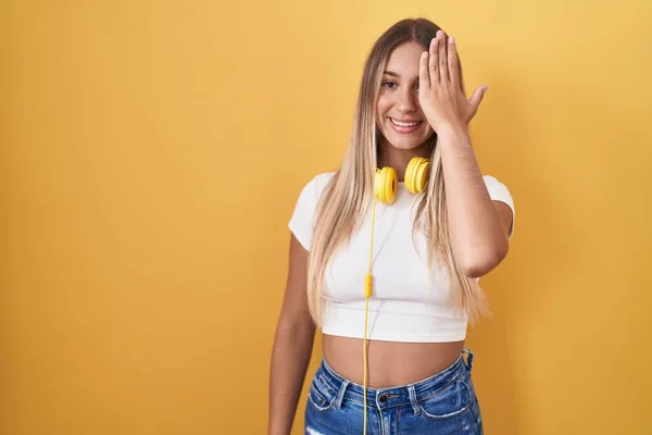 Young Blonde Woman Standing Yellow Background Wearing Headphones Covering One — Foto Stock