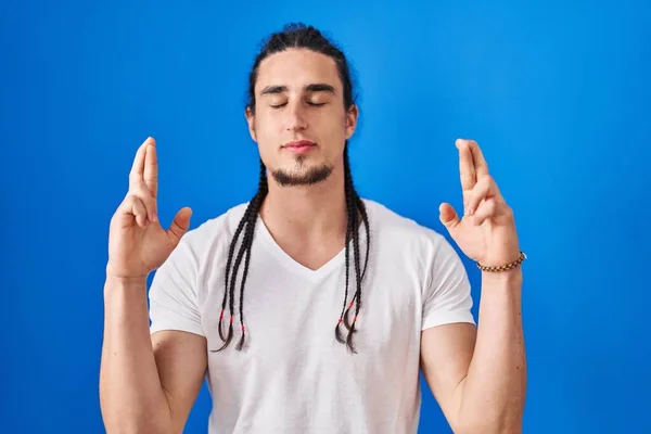 Hispanic Man Long Hair Standing Blue Background Gesturing Finger Crossed — Stock fotografie