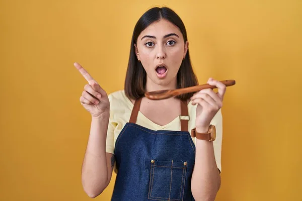 Hispanic Girl Eating Healthy Wooden Spoon Surprised Pointing Finger Side — Zdjęcie stockowe