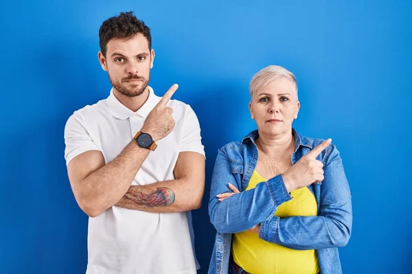 若いですブラジルの母親と息子立ちます上の青の背景を指しています手指で側面に示す広告 深刻かつ穏やかな顔 — ストック写真