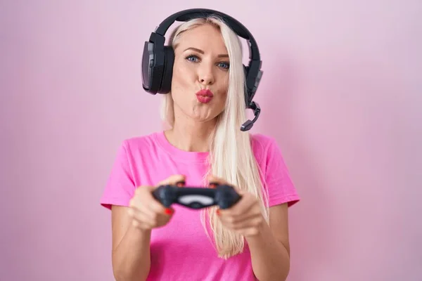 Caucasian woman playing video game holding controller looking at the camera blowing a kiss being lovely and sexy. love expression.