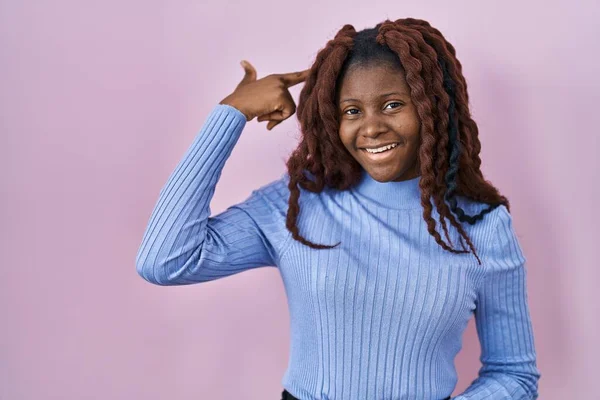 Африканская Женщина Стоит Розовом Фоне Улыбаясь Указывая Голову Одним Пальцем — стоковое фото