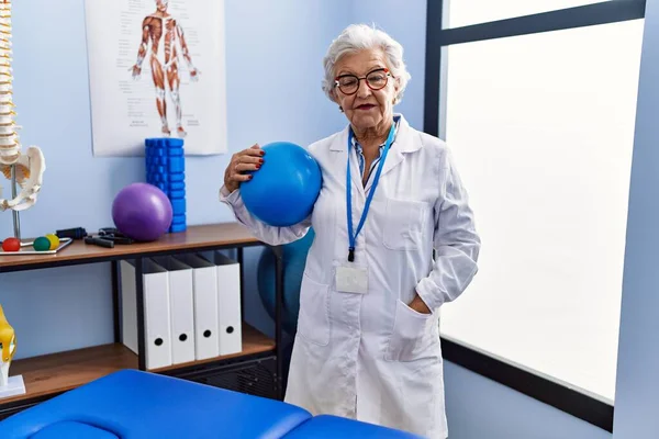 Starsza Siwowłosa Kobieta Mundurze Fizjoterapeuty Trzymająca Piłkę Klinice Fizjoterapii — Zdjęcie stockowe