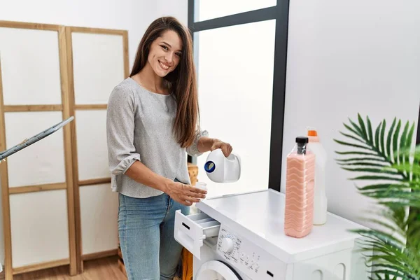 年轻的黑发女人在洗衣机里放洗涤剂 脸上挂着快乐而清凉的笑容 显示牙齿 — 图库照片