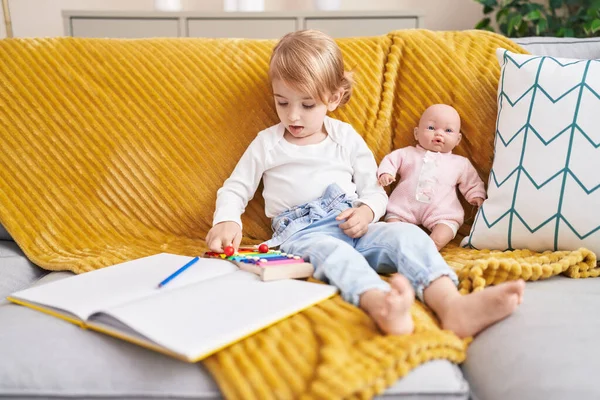 Ksilofon Çalan Sevimli Beyaz Kız Evde Oyuncak Bebekle Kanepede Oturuyor — Stok fotoğraf