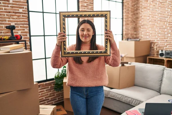 Young Latin Woman Moving New Home Holding Empty Frame Winking — Foto de Stock