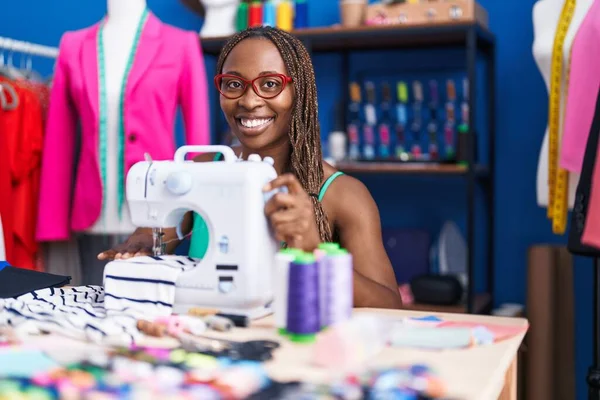 African american woman tailor smiling confident using sewing machine at atelier