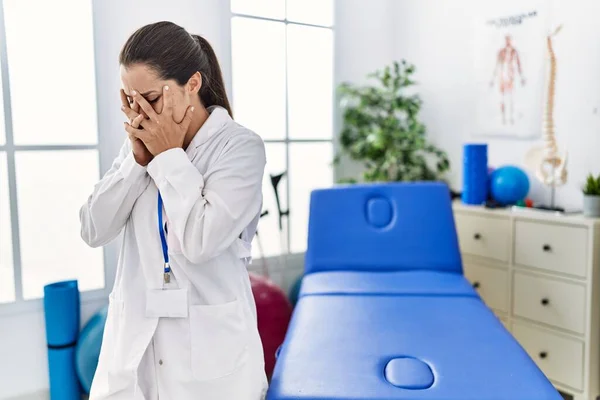 Young doctor woman working at pain recovery clinic with sad expression covering face with hands while crying. depression concept.