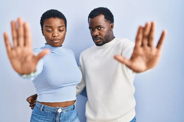 Stock image Young african american couple standing over blue background doing stop sing with palm of the hand. warning expression with negative and serious gesture on the face. 