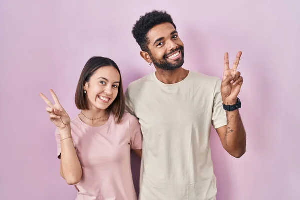 Young Hispanic Couple Together Pink Background Smiling Happy Face Winking — 图库照片