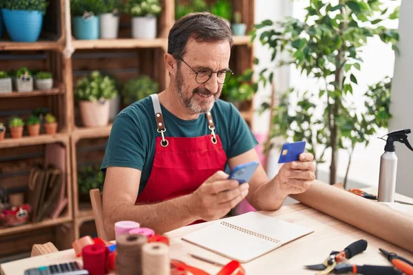 Middle age man florist using smartphone holding credit card at florist