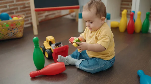 幼稚園の床に座っている車のおもちゃで遊ぶ愛らしいヒスパニック系の赤ちゃん — ストック写真