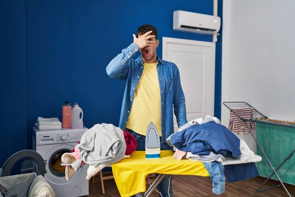Young Hispanic Man Ironing Clothes Home Peeking Shock Covering Face — Stock Photo, Image
