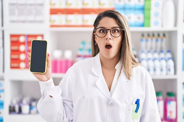 Блондинка Работающая Аптеке Показывает Экране Смартфона Испуганный Изумленный Открытым Ртом — стоковое фото