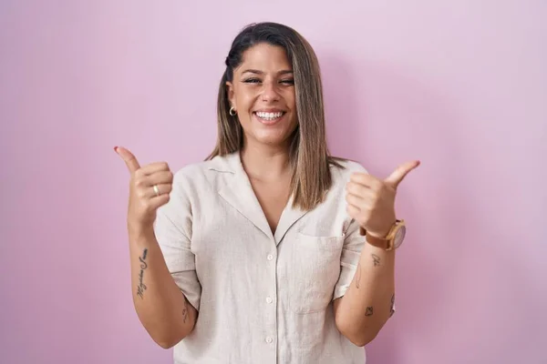 Blonde woman standing over pink background success sign doing positive gesture with hand, thumbs up smiling and happy. cheerful expression and winner gesture.