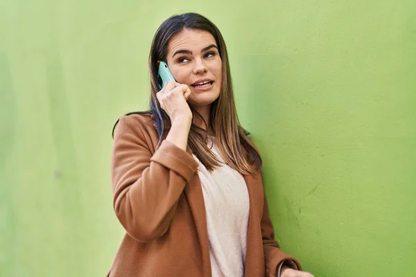 若いです美しいですヒスパニック女性笑顔自信を持って話して上のスマートフォン上で隔離された緑の背景 — ストック写真