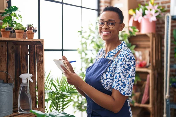 African american woman florist smiling confident writing on notebook at florist