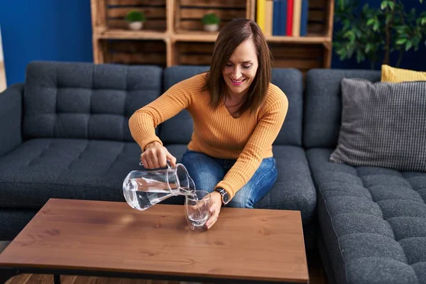 Middle age woman pouring water sitting on sofa at home