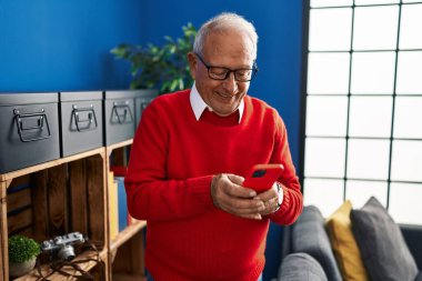 Kıdemli adam evde akıllı telefon kullanarak kendinden emin gülümsüyor.