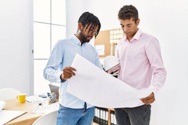 Mimarlık stüdyosunun önünde duran planlı iki mimar.