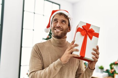 Evde kendine güvenen genç İspanyol adam Noel hediyesini tutuyor.
