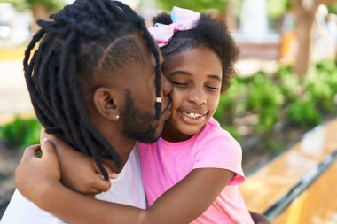 Baba ve kızı gülümsüyor. Birbirlerine sarılıyorlar ve parkta öpüşüyorlar.