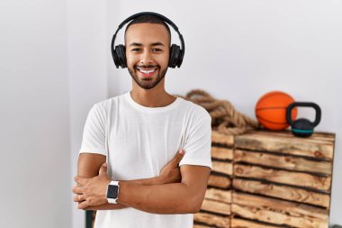 African american man listening to music using headphones at the gym happy face smiling with crossed arms looking at the camera. positive person. 