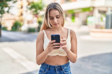 Sokakta akıllı telefon kullanan genç sarışın kadın.