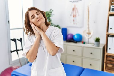 Orta yaşlı fizyoterapist kadın ağrı kesici kliniğinde çalışıyor. Uyuyor, hayal kuruyor, elleriyle poz veriyor ve gözleri kapalı gülümsüyor.. 
