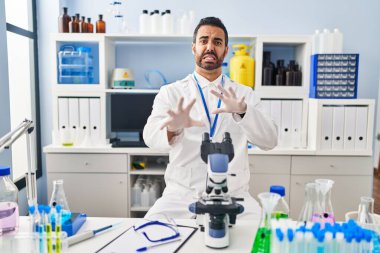 Sakallı, bilim adamının laboratuarında çalışan, tiksindirici ve tiksindirici ifadeli, tiksindirici bir genç adam. Eller havada. 