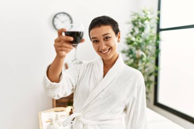 Genç İspanyol kadın bornoz giyip güzellik merkezinde şarap içiyor.