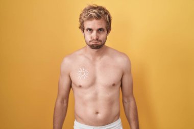 Caucasian man standing shirtless wearing sun screen puffing cheeks with funny face. mouth inflated with air, crazy expression. 