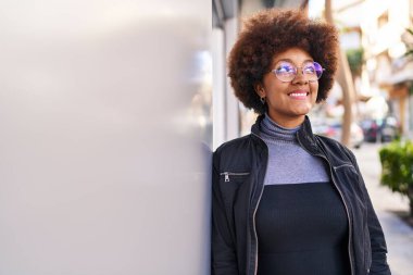 Afro-Amerikalı kadın gülümsüyor. Kendinden emin bir şekilde caddeye bakıyor.