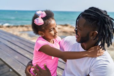 Baba ve kızı gülümsüyor. Deniz kenarında birbirlerine sarılıyorlar.