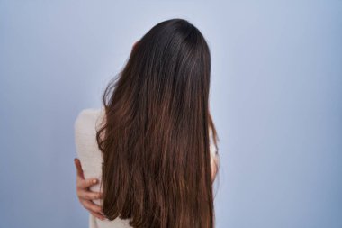 Genç esmer kadın mavi arka planda dikilip kendine sarılıyor mutlu ve pozitif bir şekilde. Sevgi ve özgüven. 