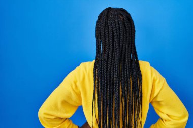 Beautiful black woman standing over blue background standing backwards looking away with arms on body 