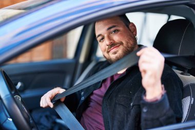 Young hispanic man wearing belt sitting on car at street