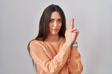 Beyaz arka planda duran esmer bir kadın sembolik bir silahla el hareketleriyle cinayet silahlarıyla oynuyor, kızgın bir yüz ifadesi var. 