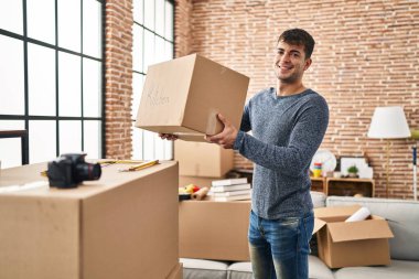 Genç İspanyol adam yeni evinde kendine güvenen bir paket tutuyor.