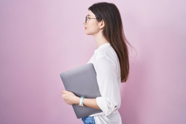 Young caucasian woman holding laptop looking to side, relax profile pose with natural face and confident smile. 