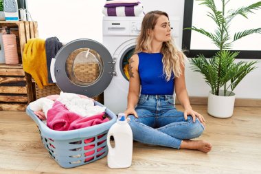 Çamaşır sepetinin yanında oturan genç ve güzel bir kadın. Yan tarafa bakıyor, rahat bir poz veriyor. Kendine güvenen bir gülümsemesi var.. 