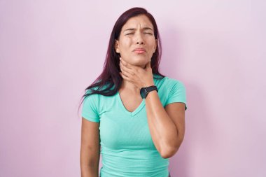 Pembe arka planda duran genç İspanyol kadın ağrılı boynuna dokunuyor, boğazı ağrıyor grip, mantar ve enfeksiyon kapmış. 