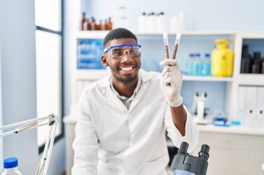 Young african american man wearing scientist uniform holding test tubes at laboratory