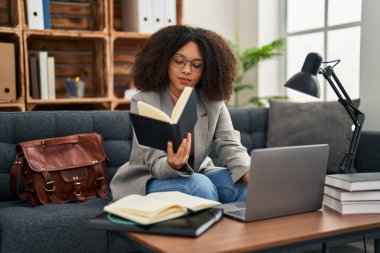 Young african american woman psychologist using laptop and reading book at psychology center
