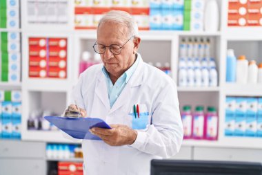 Eczanedeki belgeye yazan kıdemli gri saçlı eczacı.