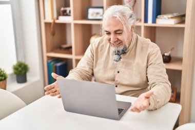 Middle age grey-haired man having video call sitting on table at home